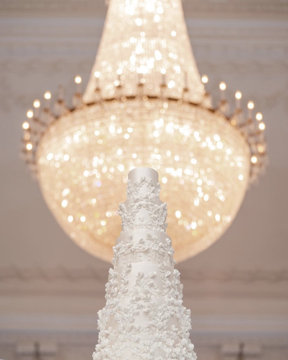 Tall white wedding cake with sugar flowers beneath a crystal chandelier