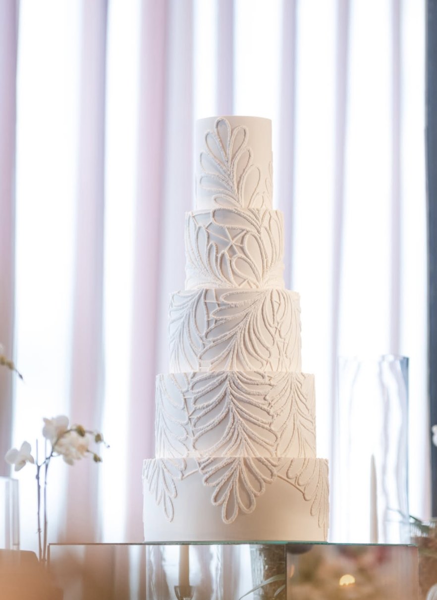 Five-tier white wedding cake with hand-piped leaf patterns