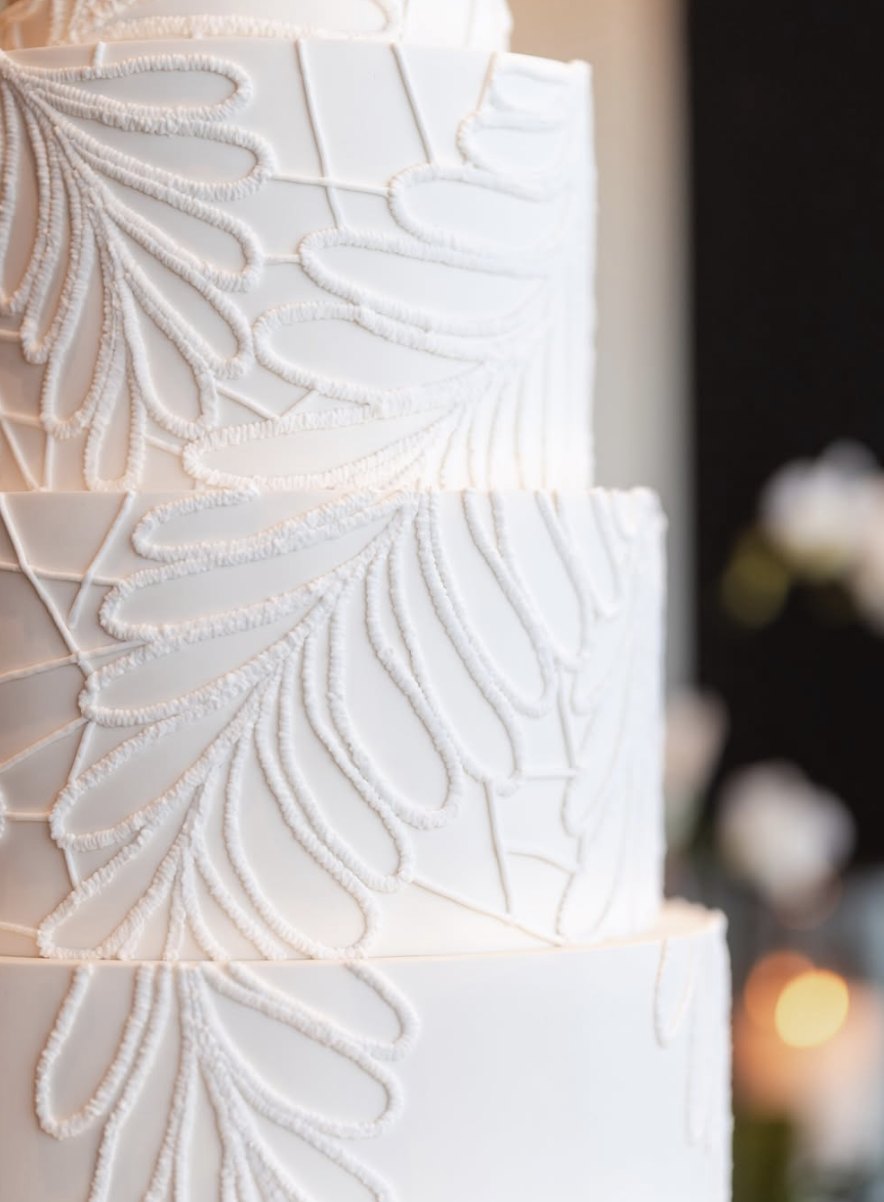 Detalle del encaje botánico hecho a mano con manga en un bizcocho de boda blanco