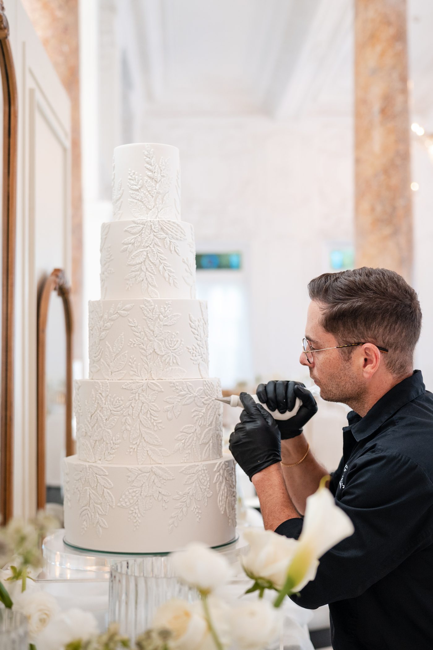 Cake designer Gabriel Díaz hand-piping leaf details on a five-tier white wedding cake